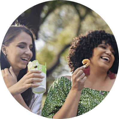 Two women laughing together while enjoying food and a drink outdoors
